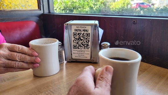 Drinking coffee while waiting for food and getting ready to scan digital menu with cellphone.