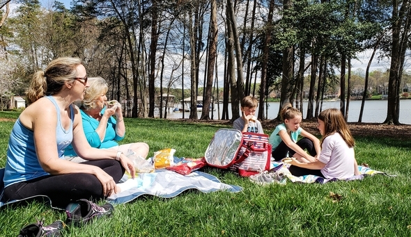 Family picnic with generation z kids on blanket lakeside in grass enjoying Lakeview.