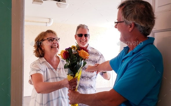 Happy couple bring gift of flowers to their friend at housewarming to home sweet home through door.