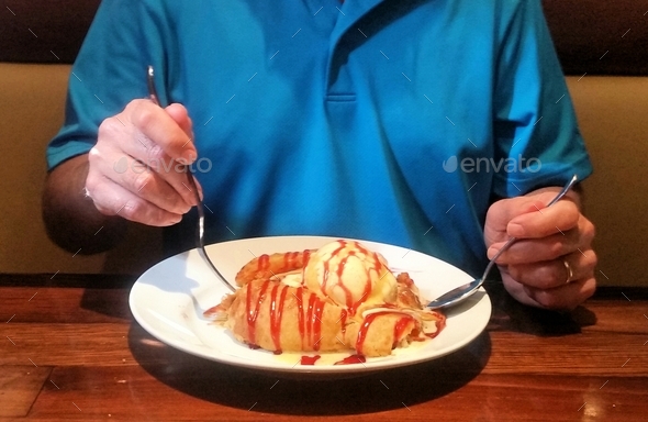 Man in blue eating an apple pie topped with vanilla icecream.