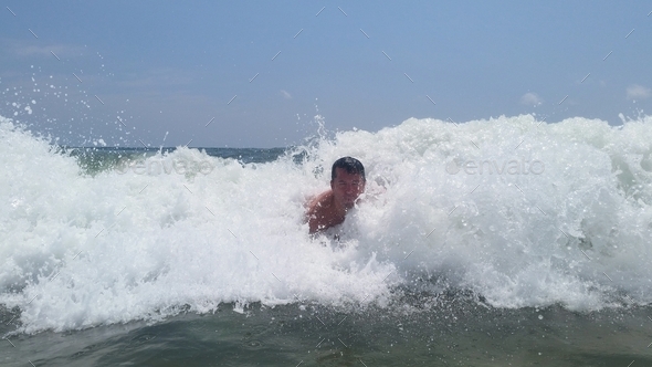 Young millennial is body surfing an ocean wave at sea with a big splash in beach landscape.