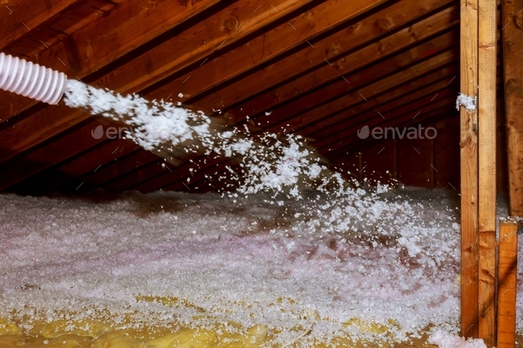 Worker Spraying mineral rock wool of thermal insulation layer under the roof house attic insulation