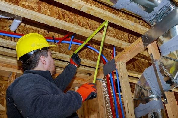 Male builder measuring plastic pipes with new home construction in hot and cold blue and red pex - Stock Photo - Images