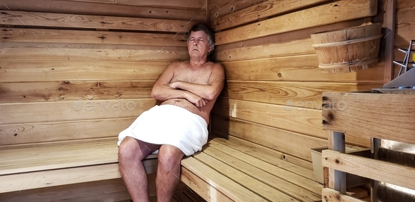 Senior Man relaxing in sauna in spa wrapped in a white towel asleep.