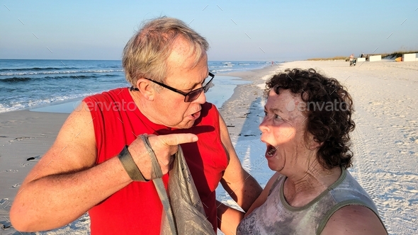 Active baby boomer couple with faces and emotions of argument and accusations on beach.