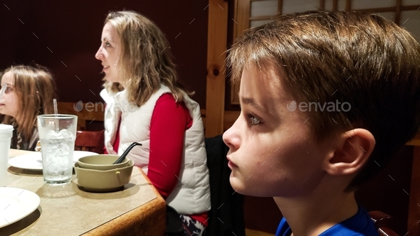 Generation z kid in deep thought sitting at head of table in restaurant waiting for food.
