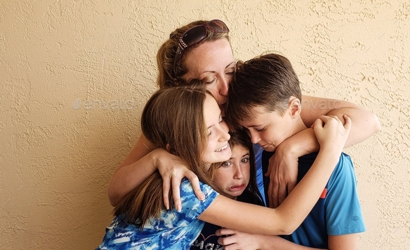 Millennial mom hugs her generation z kids with a kiss of loving tenderness in candid family.