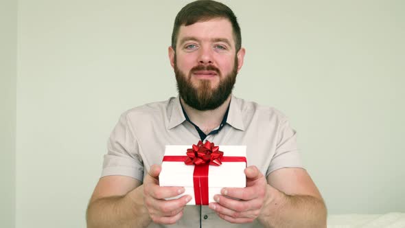 Smiling bearded man presenting gift box and looking to the camera.