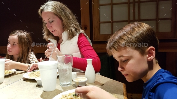 Millennial mom at table in restaurant with her generation z kids focused on eating and drinking.