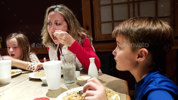 Millennial mom eating in restaurant with generation z kids focused on eating and drinking.