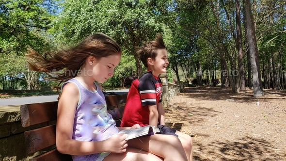 Generation z twins in the park in summertime after school doing a book report and fun.