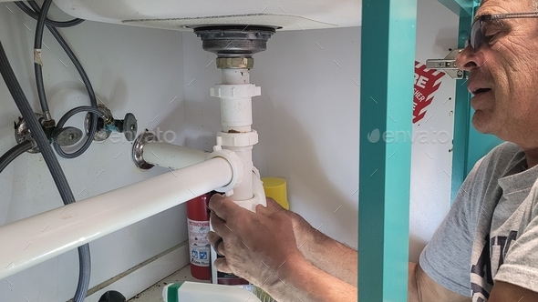 Professional Plumber working on kitchen utilities under sink stopping a water leak in repairs.