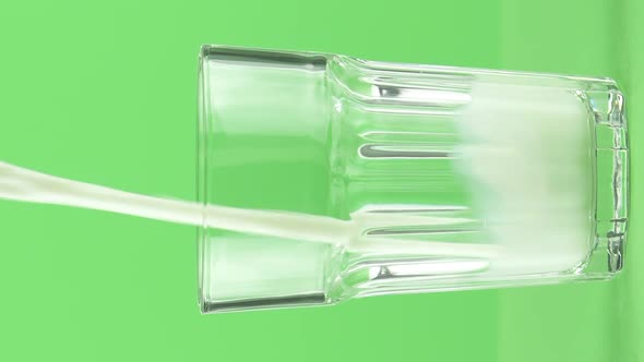 Vertical Video Milk Pouring Into Faceted Glass Close Up Isolated on Light Green Background