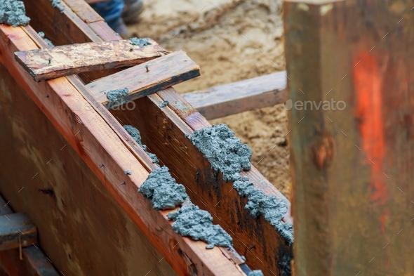 Closeup of foundation excavation with fresh poured concrete and embedded steel reinforcement bars to