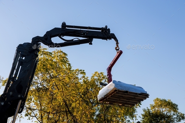 A crane lifting and moving pallet materials to home building roof