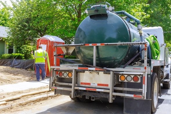 Sewage truck on worker pumping feces out of rental toilet for disposal and cleaning at the