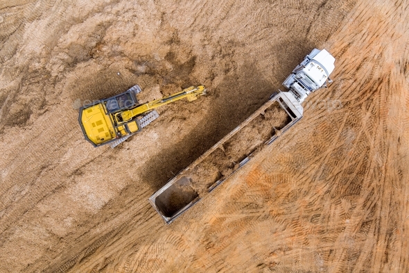 Aerial view at excavator and trucks working on the excavation works of a road, moving earth it onto