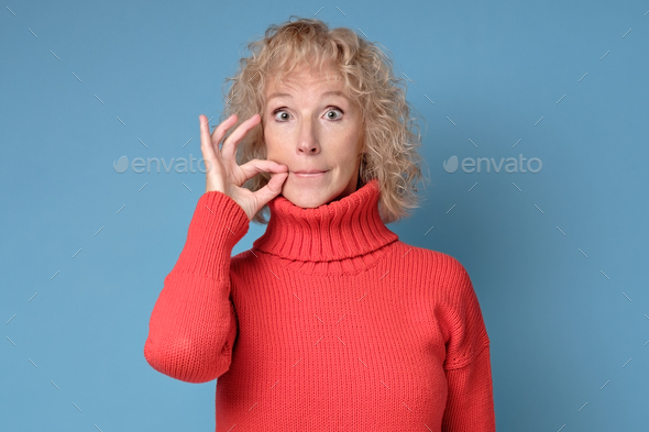 Caucasian mature woman shutting mouth and lips shut as zip with fingers.