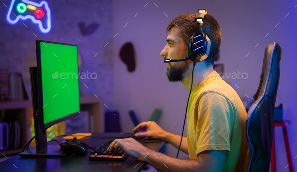 Pro gamer streaming video games with green screen mock-up display in gaming home studio. Chroma key.