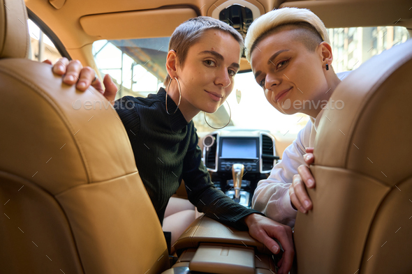 LGBT female couple in salon car, women sit on front seats half-turned