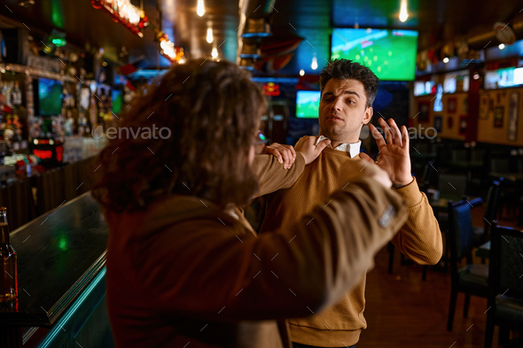Two angry friends quarreling with each other fighting at sport bar