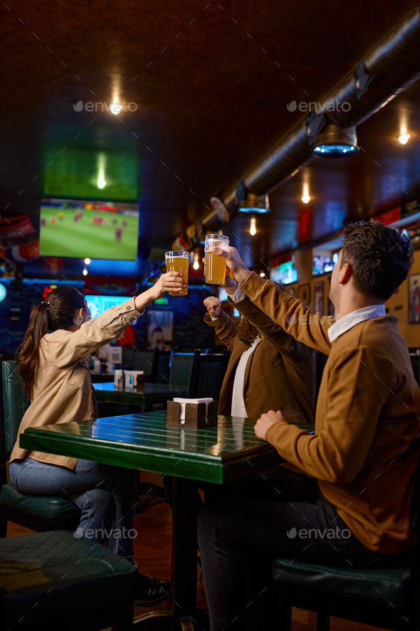 Friends watching football match clinking beer mug rest in sport bar - Stock Photo - Images