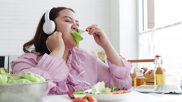 Happy Overweight woman on diet eating vegetable salad in modern kitchen at home