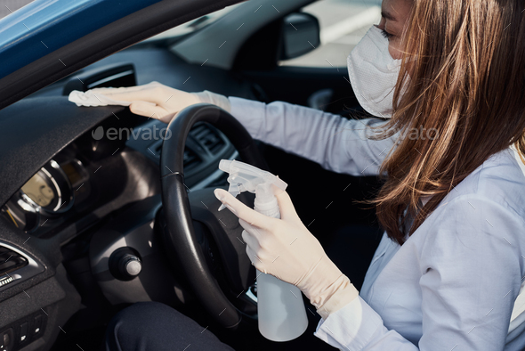 Woman cleaning a car with disinfection spray to protect from coronavirus