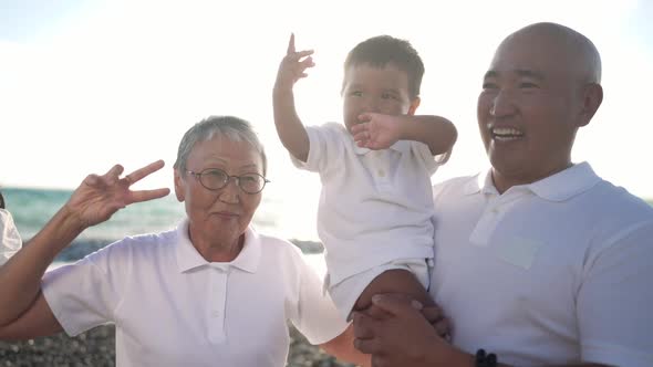 Joyful Asian Greatgrandmother Grandfather and Baby Boy Dancing in Sunlight at Mediterranean Sea alt