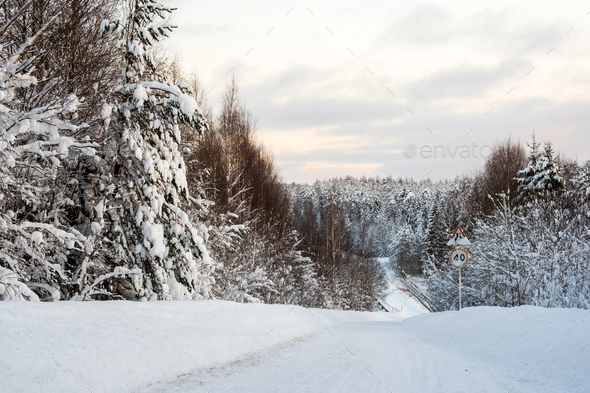 Country road cleared of snow with a steep descent down to a bridge with a frozen lake