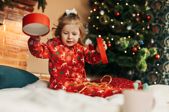 Little girl opens a Christmas present near the Christmas tree - Stock Photo - Images