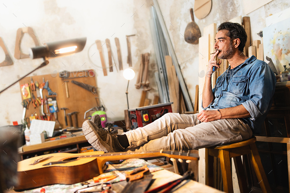 A carpenter relaxes sitting on a stool by placing his feet on the work table of his vintage woodwork