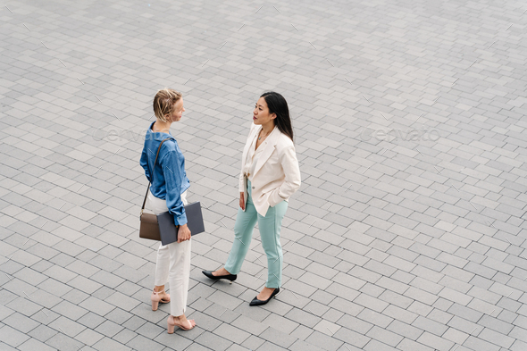 Two young business women talking and having work conversation outdoors in a cobblestone street