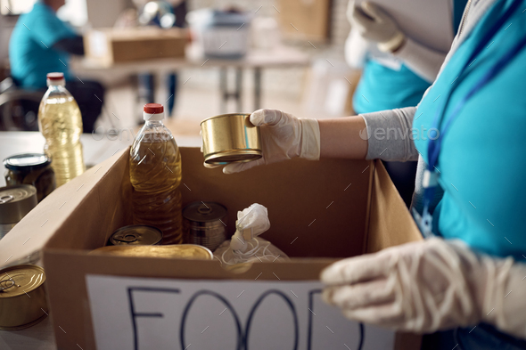 Close-up of woman packing food in donation boxes while volunteering at charitable foundation.