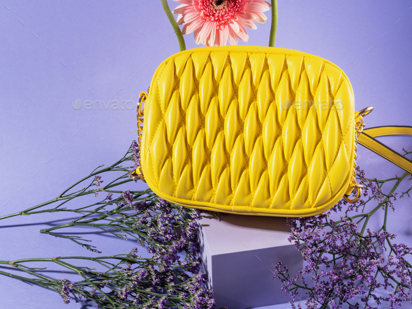 Yellow fashion lady handbag with pink flowers on purple podium