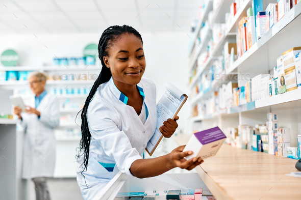 Young smiling black pharmacist going through inventory in a pharmacy.