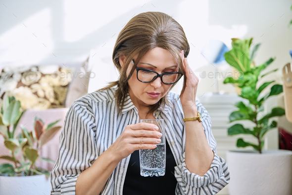 Mature woman suffering from headache, at home with glass of water - Stock Photo - Images