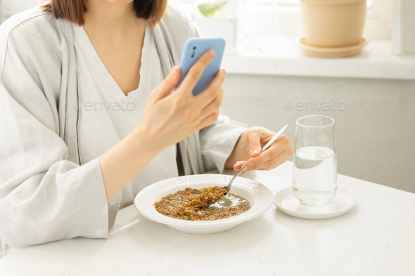 Caucasian woman eats lunch with her phone in her hands,eating and being distracted by social media