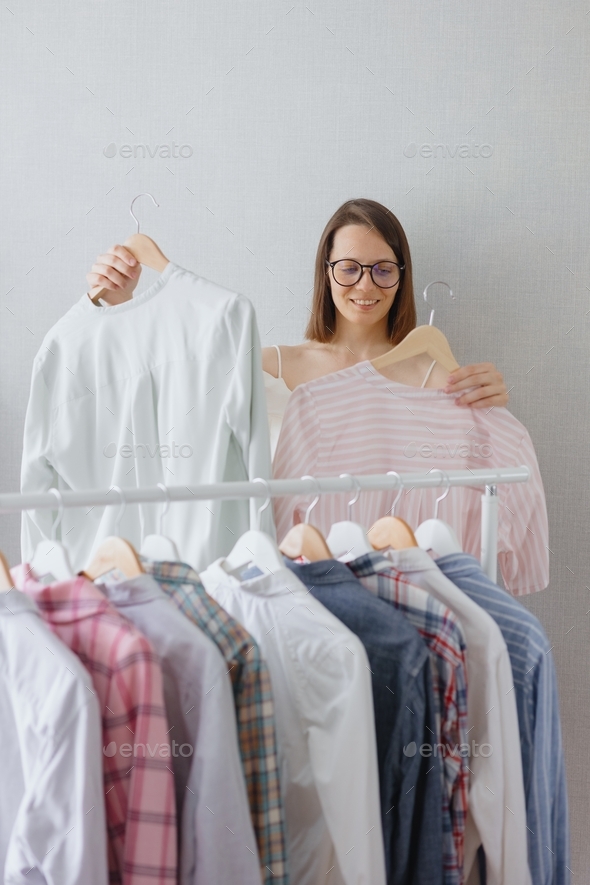 beautiful and young adult European woman stylist choose clothes in her closet.