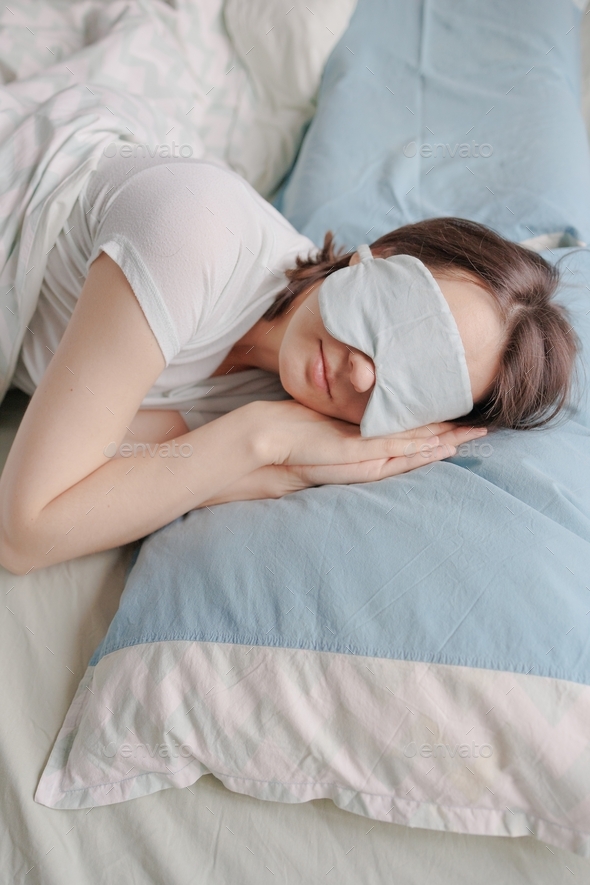 a European woman with dark hair in bed with a mask over her eyes can't fall asleep