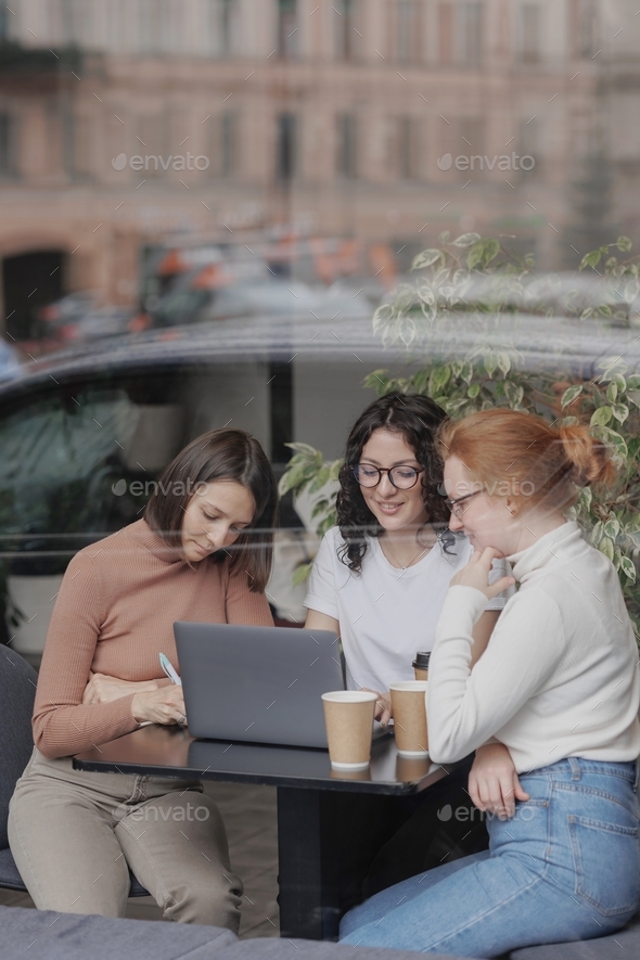three female friends are drinking coffee and discussing a project a job. self-confident millennial