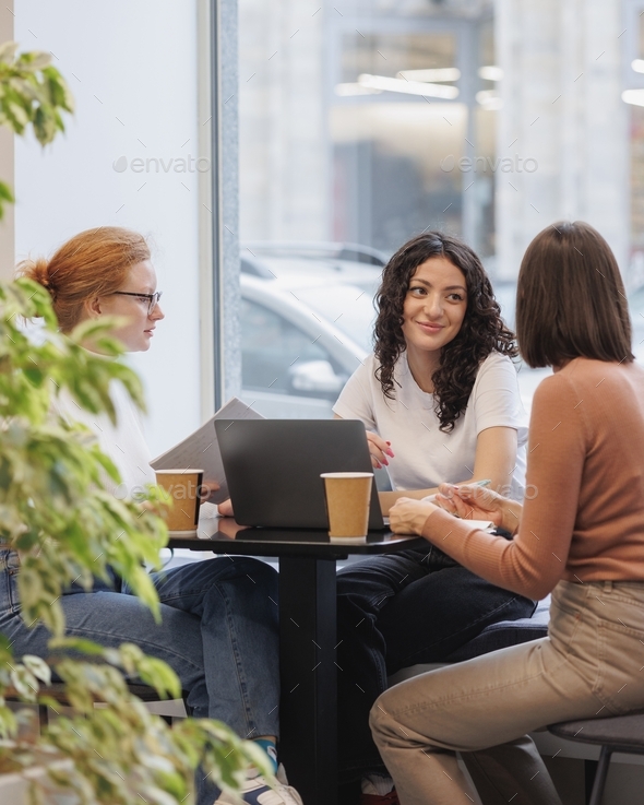 three European young female student friends who are drinking coffee, discussing a project or a job