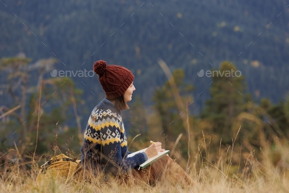  woman in the mountains on guard is resting and taking notes in a notebook or writing a travel diary