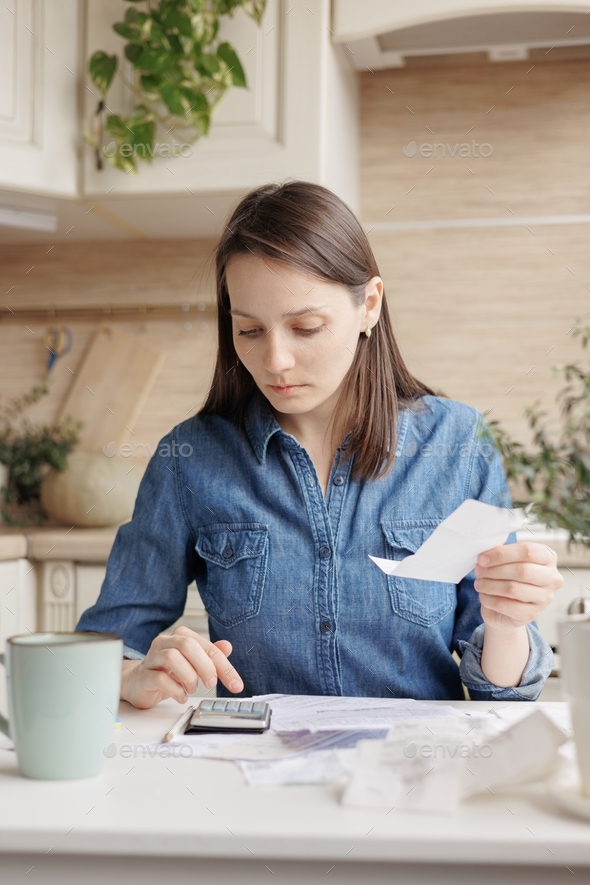 woman sits at the kitchen table and pays utility bills and writes checks. financial literacy