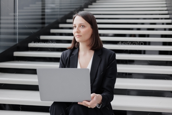 thoughtful business woman in an office or a congress center is sitting on the stairs, holding a lapt