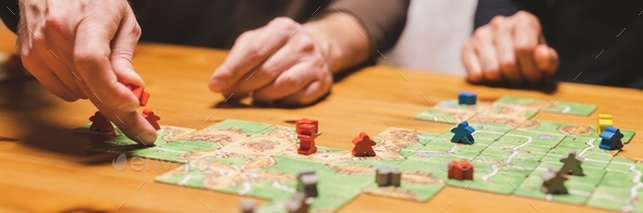 men friends have fun playing the carcassonne board game at night. male hands and game cards and chip