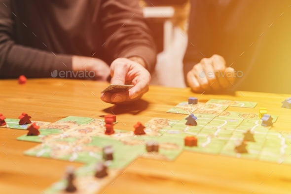 men friends have fun playing the carcassonne board game at night. male hands and game cards and chip