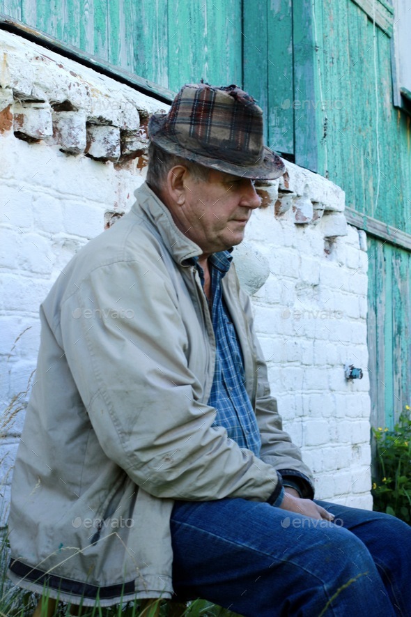 old man in a hat sitting on the porch of village house. Senior lifestyle. Leisure, country, rest