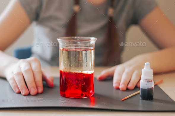 School girl doing science experiment with water, food coloring, oil and aspirin. Education.
