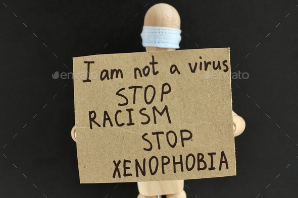 Cardboard sign with text in the hands of a wooden doll or mannequin in a medical mask. anti racism